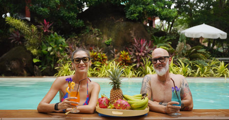 A man and a woman are having fun and drinking cocktails in the pool.