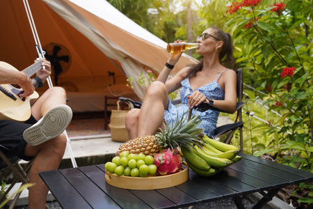 A man plays guitar for a woman near a cozy tent at a glamping site.の写真素材