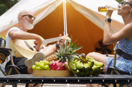A man plays guitar for a woman near a cozy tent at a glamping site.の写真素材