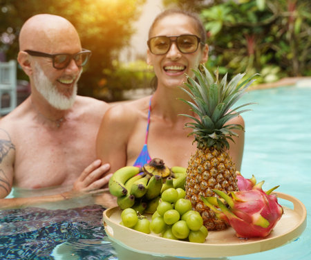 A man and woman with tray of a fresh fruits in a swimming pool