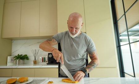 A white man cuts mango in the morning in the kitchenの写真素材