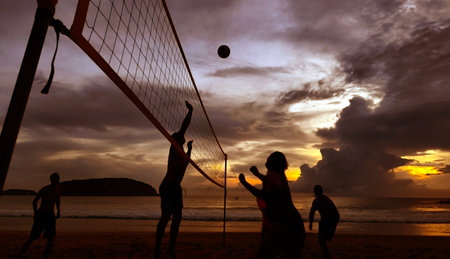 Young people playing beach volleyball by the ocean at sunsetの写真素材