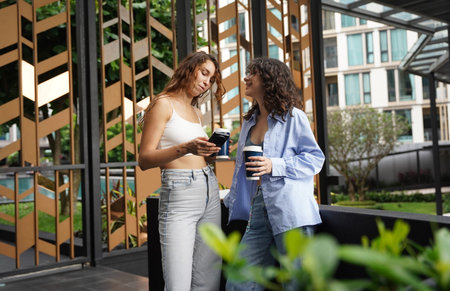 Two young women drink coffee and take pictures near the entrance to the office.