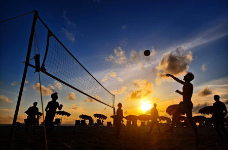 Young people playing beach volleyball by the ocean at sunsetの写真素材