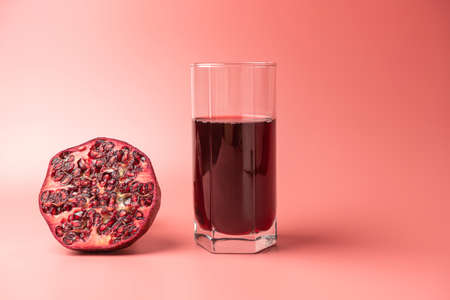 a glass of pomegranate juice and pomegranates on a red backgroundの写真素材