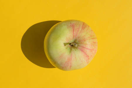 an apple with a hard shadow on a yellow backgroundの写真素材