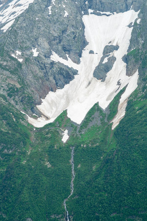 Majestic Mountain Landscape Features Snow, Green Valleys, and a Waterfallの写真素材