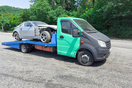 Truck Transporting a Damaged Car on a Rural Road in Sunny Weatherの写真素材