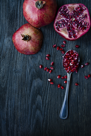 Healthy fresh pomegranates on a dark wooden background. A spoon with grains of fresh pomegranate. Vibrant focus. Dark wooden background. View from above.の写真素材