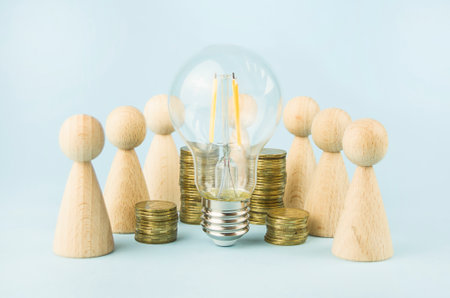 business concept. Team concept and idea creation. Wooden figures of people stand around coins and a lamp on a blue background. teamwork. Brainstorming Business Recovery and Growth. copyspace.の写真素材
