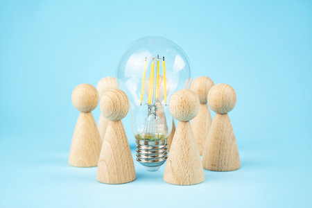 business concept. Team concept and idea creation. Wooden figures of people stand around coins and a lamp on a blue background. teamwork. Brainstorming Business Recovery and Growth. copyspace.の写真素材