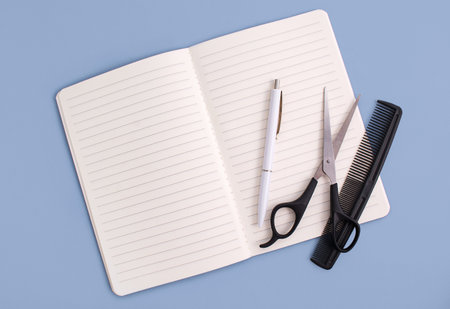 Notebook, pen and hairdressing tools on a blue background. Appointment to the hairdresser. The concept of a hairdresser, beauty salon, tools. copyspace. view from above.の写真素材