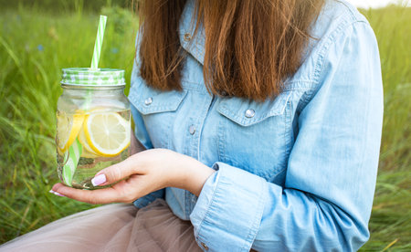 A girl holds a glass with a cooling drink at sunset. outdoor recreation. copy spaceの写真素材