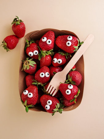 Halloween food. Scared strawberries with eyes in a food container with a fork on a light background. creepy food. Halloween background. view from above. close-up.の写真素材