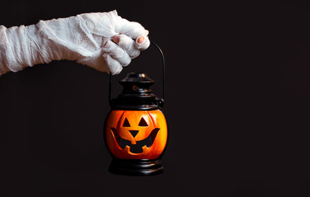 Halloween background. Zombie hand holding a lantern in the form of a pumpkin on a dark background. Halloween design. Copy space.