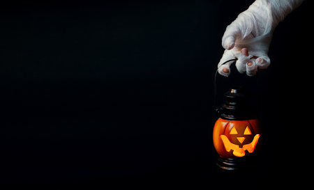 Halloween background. Zombie hand holding a lantern in the form of a pumpkin on a dark background. Halloween design. Copy space.の写真素材