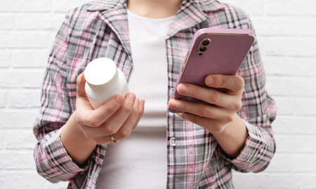 A woman holds a jar of pills and a phone in her hand. Flu medicine, pain reliever, vitamins. Concept...