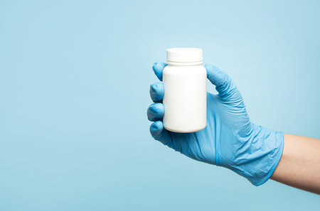 A hand in a medical glove holds a white jar for pills and supplements. Mockup. Medicine concept.