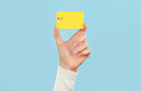 A female hand holds a payment card on a blue background. Bank card layout.の写真素材
