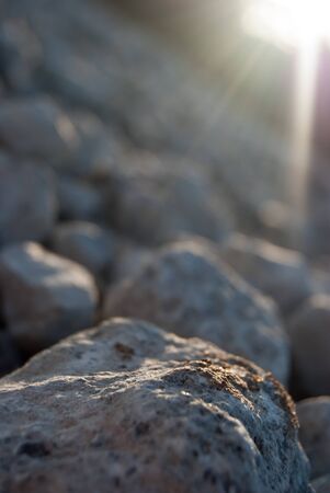 stones under sun rays at dusk on stony beach near seaの写真素材