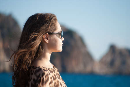 woman in sunglasses, profile, against sea and rocksの写真素材