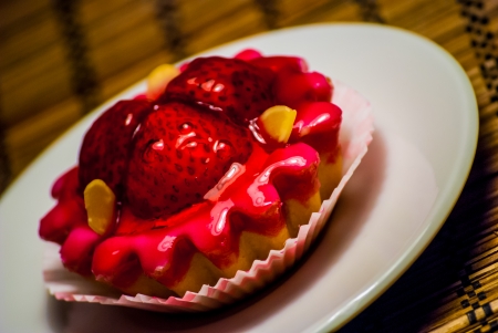 red cupcake on a white plate on wooden matの写真素材