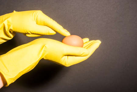 Female hand in robber glove pointing to brown egg against black backgroundの写真素材