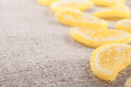 Marmalade pieces in shape of lemon slices on rough textile. Sweet food background.