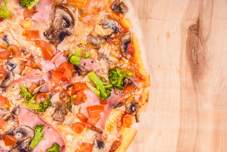 pizza with mozzarella,  ham, mushrooms chicken, broccoli, and tomatoes, whole, uncut, on wooden tableの写真素材