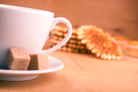 white china cup with brown sugar, cookies, and muffins on tableの写真素材