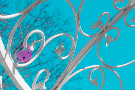 white forged plant ornament with purple padlock against blue skyの写真素材