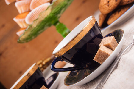Blue china cup with brown sugar, cookies, and muffins on tableの写真素材