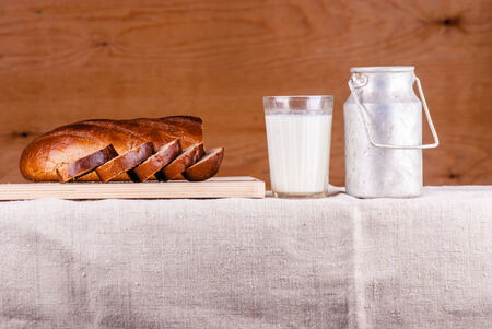 Cut loaf of fresh bread on burlap and glass of milk against woodの写真素材