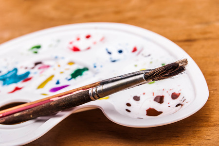 White plastic art palette with random watercolor paint blobs and brushes on woodの写真素材