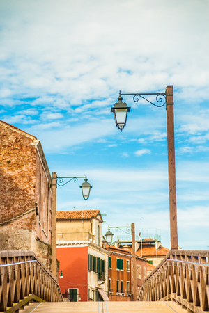 Beautiful colorful image of a street (Fondamenta SantAnna) in Venice with a bridge, old houses, lanterns, and cloudy sky above.の写真素材