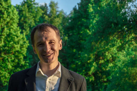 Young man in formal outfit looking with smile in camera, outdoors on the green background. Business man in a green zone or park. An image for topics of finance and business.の写真素材