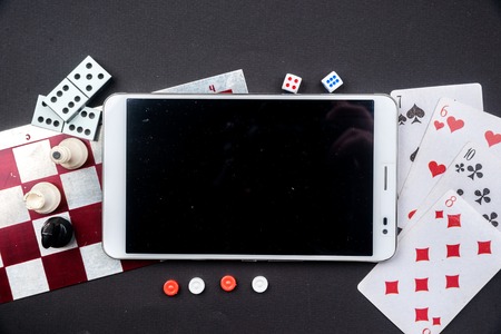 Various board games and figurines with tablet pc over checkers board and dark background. Metaphor for computer gaming and online gambling.の写真素材