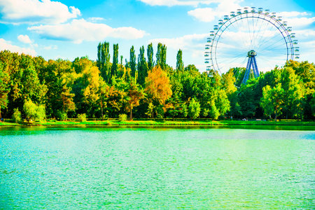 Big ferris wheel in city park. Beautiful landscape with lake, trees blue sky, and cloudsの写真素材