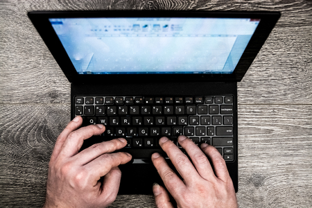 Black laptop on wood with hands viewed from above.の写真素材