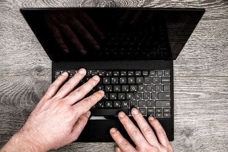 Black laptop on wood with hands viewed from above.