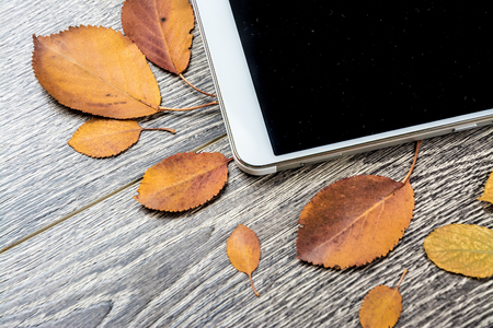 White modern tablet pc with blank empty screen on rustic vintage wood background with autumn leaves. Concept of season and technology, nature and computrs design template with place for image and textの写真素材