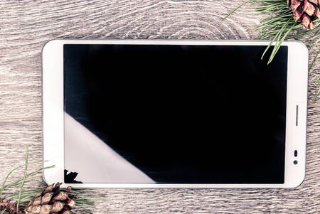 Tablet pc with blank screen and christmas fir tree with cones on a wooden background. Template for banner or bavkground, or image for a blog.の写真素材