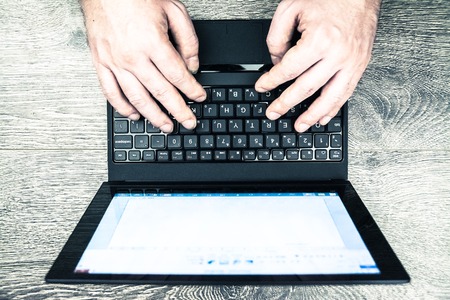 Black laptop on wood with hands viewed from above.の写真素材