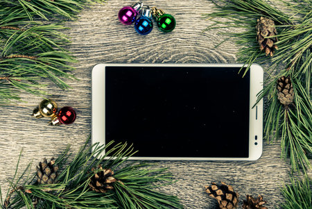 Tablet pc with blank screen and christmas fir tree with cones and christmas tree decoration on a...