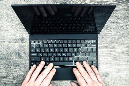 Black laptop on wood with hands viewed from above.の写真素材