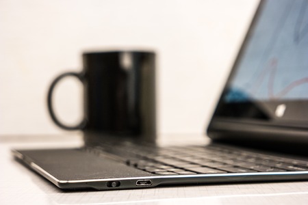 Black laptop with business charts on screen, on white table in office. With coffe cup in background.の写真素材