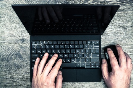 Black laptop on wood with hands viewed from above.の写真素材