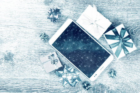 Tablet computer with blank black screen among christmas gifts on wooden background. Holiday image...