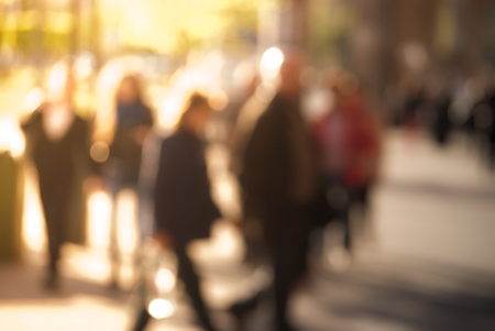 People walking down the street in the evening, beautiful light at sunset. The photo is purposely made out of focus, no faces are recognisibleの写真素材