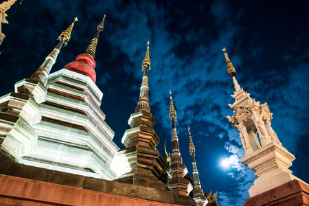 Night view of a temple in Chiang Mai, Thailand, with clouds flying in front of the moon.の写真素材